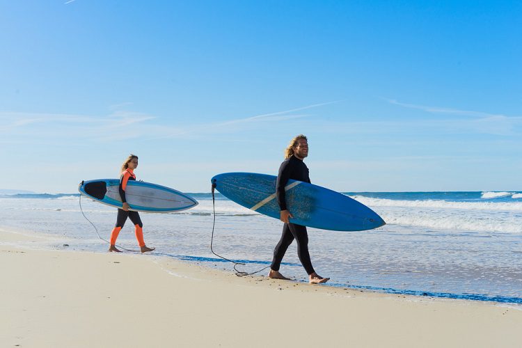 man and woman carrying surfboards into the calm ocean water - beginner surf spots in San Diego