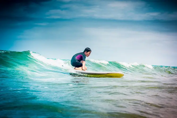 Teen boy surfing on a small wave with yellow surf board - best beginner surf spots in San Diego