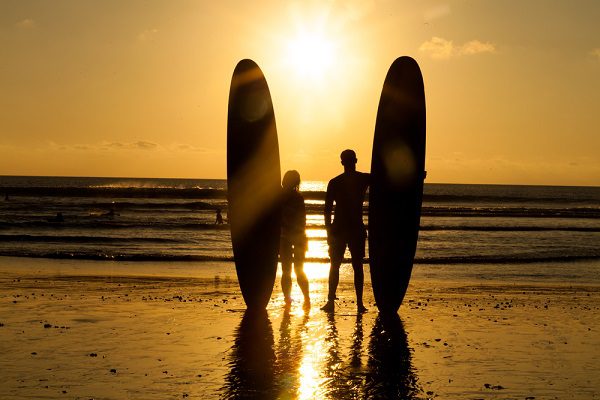 two surfers holding surfboards looking into the ocean at sunset - best foam surfboards for beginners 