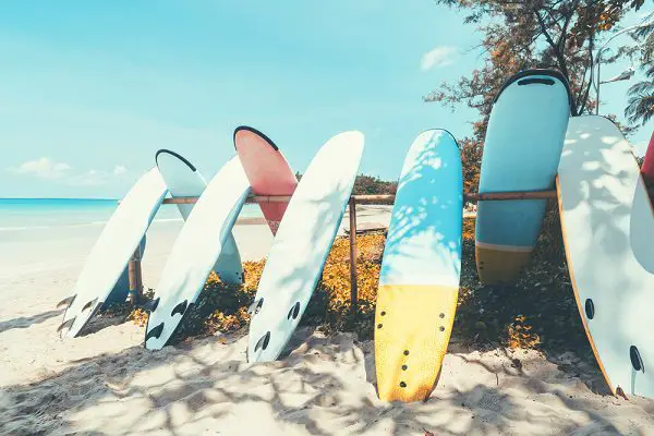 seven colorful surfboards leaning on a rack on sandy beach