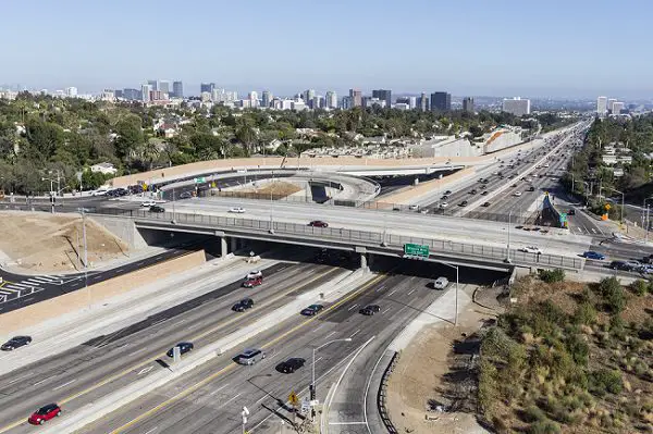 Aerial view of San Diego freeway plus two interchanges with moderate traffic and the city skyline in the background 