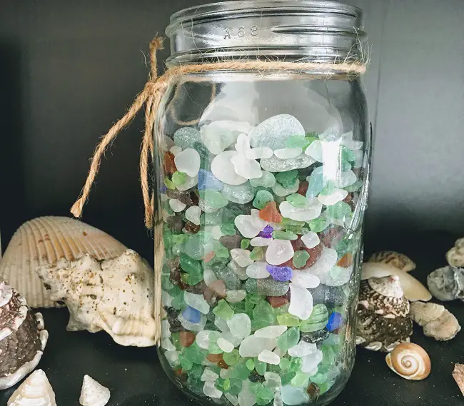 jar full of colorful sea glass on shelf with sea shells